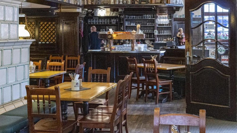 Cozy interior of a restaurant with wooden tables and chairs, a bar in the background and a large tiled stove on the left., &copy; SMG Stuttgart Marketing GmbH - Sarah Schmid