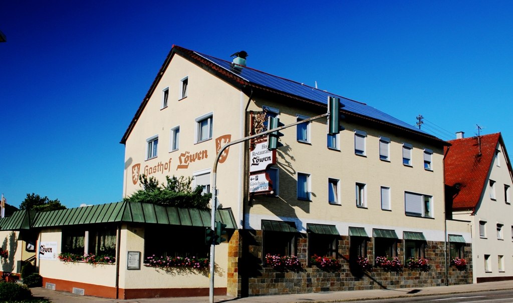 Der Gasthof Löwen mit beiger Fassade und roten Dächern, dekoriert mit Blumen, unter blauem Himmel., © Ulli Kellenbenz