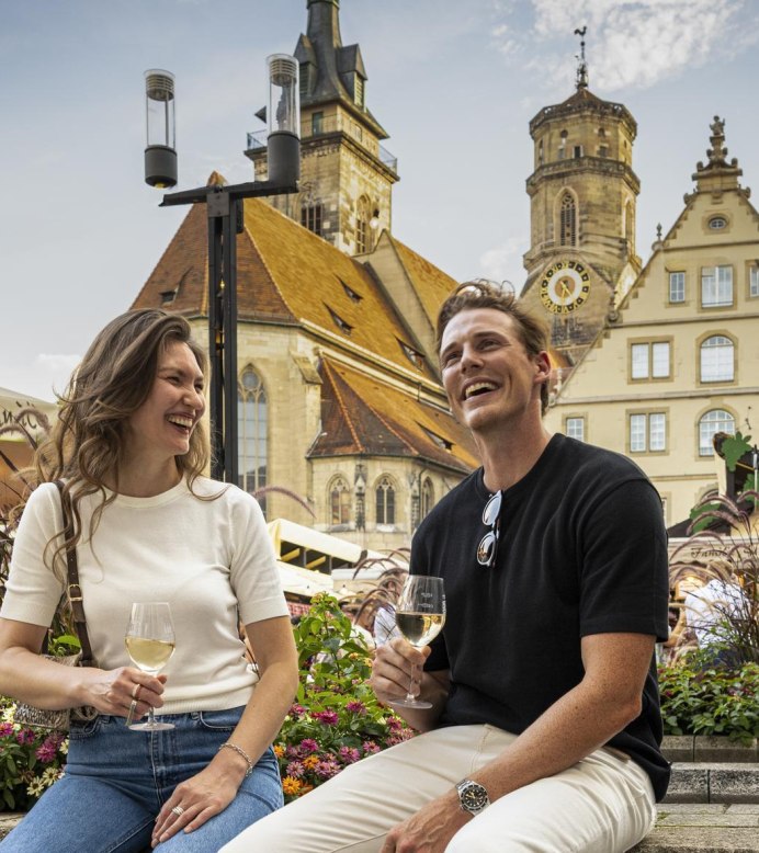 A couple enjoy the Stuttgart wine village on Schillerplatz, surrounded by flowers and historic buildings. They are both holding glasses of wine and laughing., &copy; Stuttgart-Marketing GmbH, Sarah Schmid