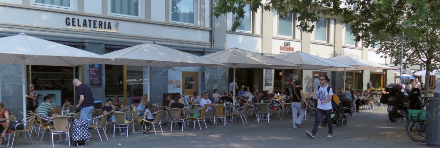 People sit under parasols in front of the Kaiserbau gelateria on Marienplatz. A few passers-by walk past., © Stuttgart-Marketing GmbH