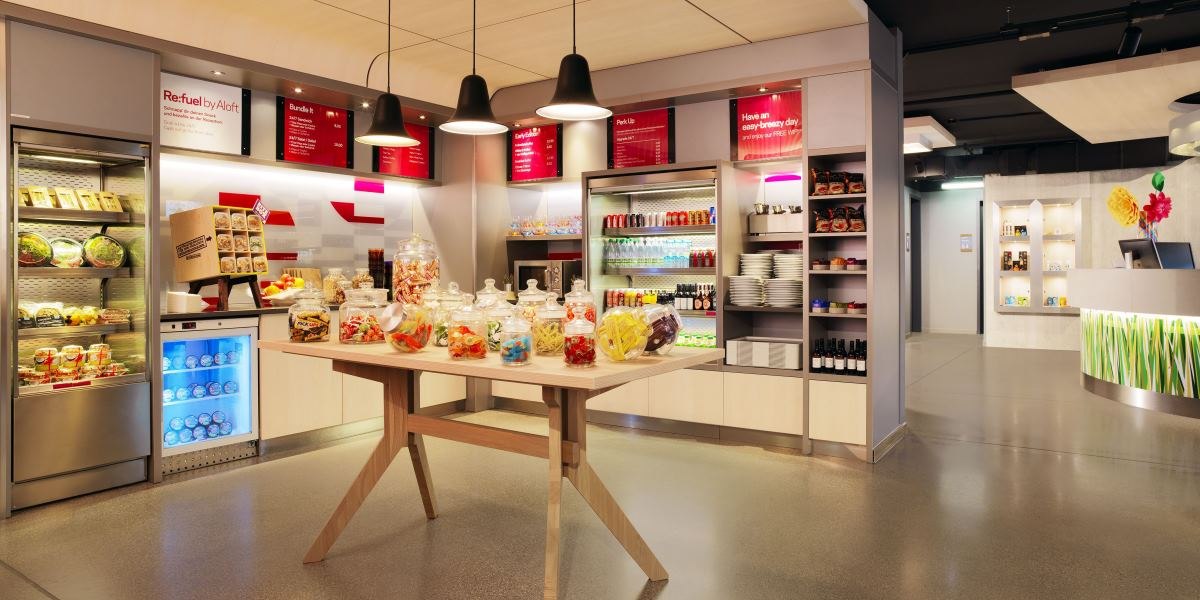 Moderner Selbstbedienungsladen mit Snacks, Getränken und Süßigkeiten in Glasbehältern. Helle Beleuchtung und stilvolle Einrichtung., © Aloft Stuttgart