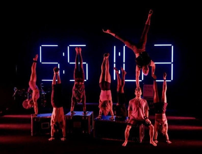 Eight acrobats do handstands on boxes in front of a glowing digital clock display in a dark room., &copy; Theaterhaus Stuttgart e.V.