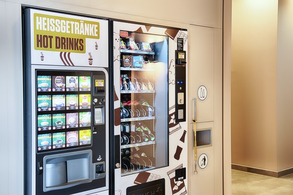 Ein Verkaufsautomat für Heißgetränke und Snacks steht in einem beleuchteten Innenraum. Links sind Getränke, rechts Snacks erhältlich., © B&B Hotel Stuttgart-Neckarhafen Ein Verkaufsautomat für Heißgetränke und Snacks steht in einem beleuchteten Innenraum. Links sind Getränke, rechts Snacks erhältlich., © B&B Hotel Stuttgart-Neckarhafen