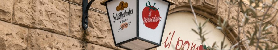 A sign with the Schöfferhofer logo and tomato motif hangs on a stone wall in front of the restaurant 'il pomodoro'., © SMG Stuttgart Marketing GmbH - Sarah Schmid