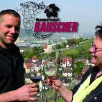 Two people toasting with wine glasses, in the background a view of the town with vineyards. Lettering "Besenwirtschaft Rauscher" and grape logo., © Besenwirtschaft Rauscher Two people toasting with wine glasses, in the background a view of the town with vineyards. Lettering "Besenwirtschaft Rauscher" and grape logo., © Besenwirtschaft Rauscher