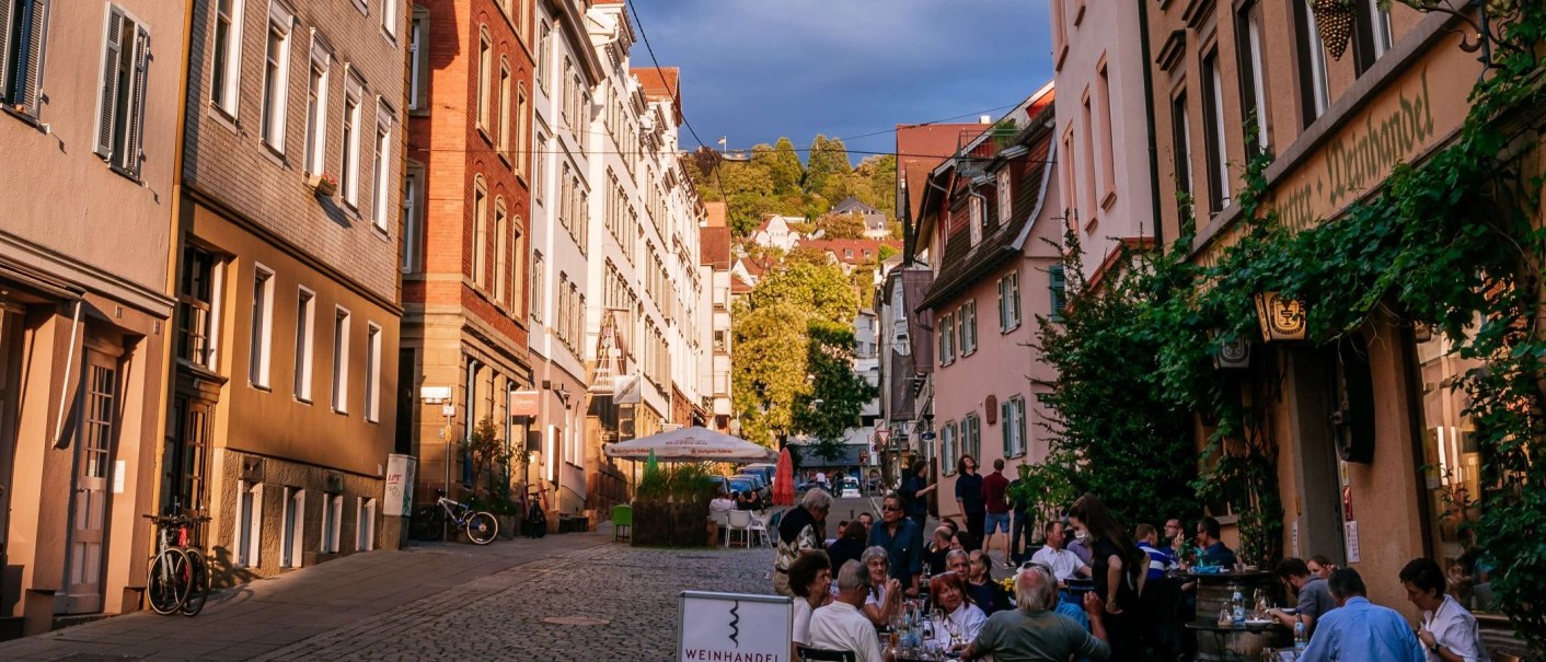Straßenszene im Bohnenviertel mit Menschen, die in einem Café sitzen. Historische Gebäude und grüne Pflanzen säumen die Straße., © Thomas Niedermüller Straßenszene im Bohnenviertel mit Menschen, die in einem Café sitzen. Historische Gebäude und grüne Pflanzen säumen die Straße., © Thomas Niedermüller