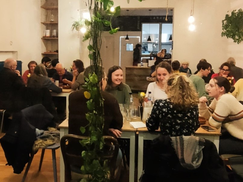 Gemütliches Café mit Menschen, die an Tischen sitzen und sich unterhalten. Pflanzen und warme Beleuchtung schaffen eine einladende Atmosphäre., © Labyrinth Gemütliches Café mit Menschen, die an Tischen sitzen und sich unterhalten. Pflanzen und warme Beleuchtung schaffen eine einladende Atmosphäre., © Labyrinth