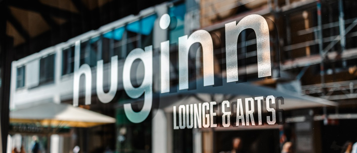 Schaufenster mit dem Schriftzug 'huginn LOUNGE & ARTS'. Im Hintergrund sind unscharf Menschen und Gebäude zu sehen., © SMG_Sarah Schmid