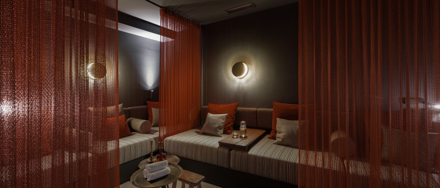 Ein gemütlicher Ruheraum mit roten Vorhängen, gedämpfter Beleuchtung und bequemen Sitzgelegenheiten. Ein Tisch mit Handtüchern und Gläsern steht bereit., © EmiLu Hotel GmbH