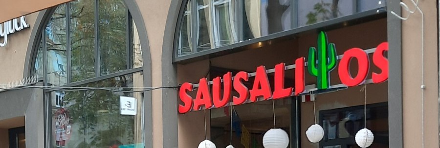 Entrance to the Sausalitos restaurant with red lettering and cactus decoration. Outdoor area with wooden tables and advertising board for Taco Tuesday., &copy; SMG