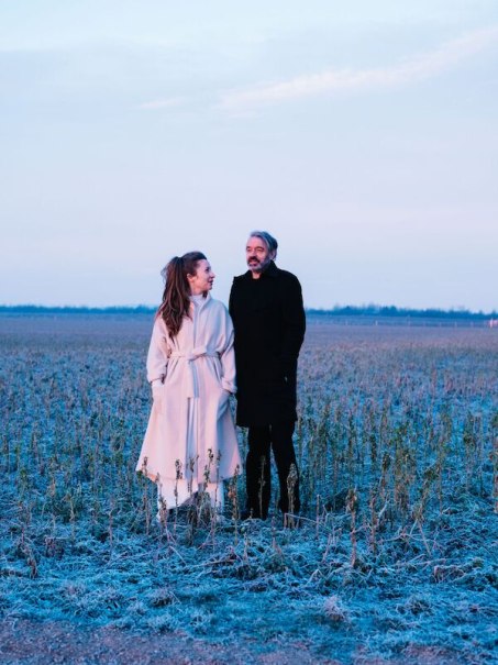 Zwei Personen in Wintermänteln stehen in einem frostigen Feld bei Sonnenuntergang. Der Himmel ist pastellfarben, die Landschaft wirkt ruhig und kalt., © Theaterhaus Stuttgart e.V. Zwei Personen in Wintermänteln stehen in einem frostigen Feld bei Sonnenuntergang. Der Himmel ist pastellfarben, die Landschaft wirkt ruhig und kalt., © Theaterhaus Stuttgart e.V.