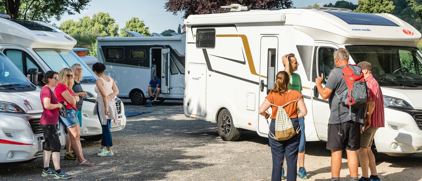Several people are chatting next to parked motorhomes on a sunny pitch., © Blu Dolci Artwork