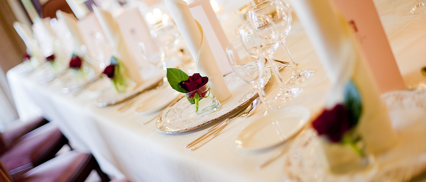 Ein festlich gedeckter Tisch mit weißen Servietten, roten Rosen und elegantem Geschirr in einem Bankettsaal., © Hotel Krone