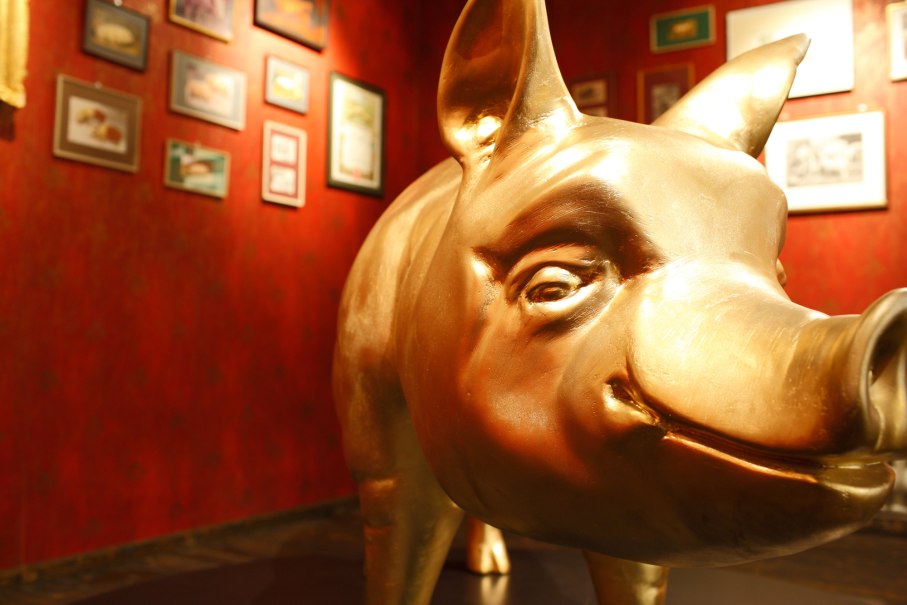 Eine goldene Schweinestatue in einem Museum. Die Wände sind rot und mit verschiedenen Bildern dekoriert., © SMG,Christoph Düpper