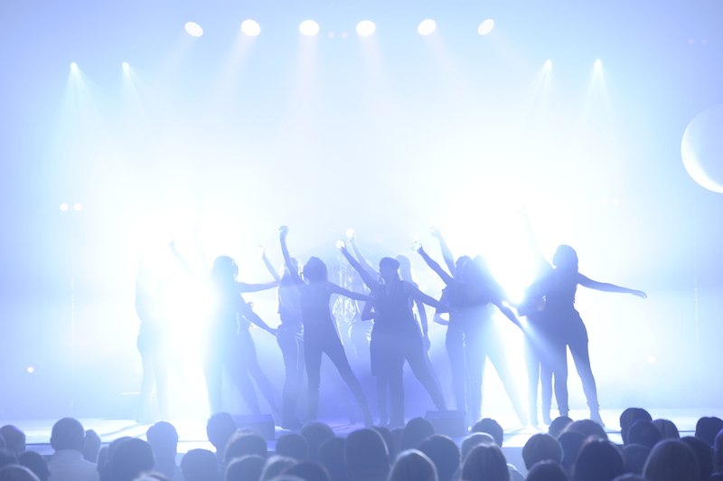 Dancers pose dramatically on a brightly lit stage while the audience looks on. The scene is characterized by intense lighting effects., © Fratelli BV Dancers pose dramatically on a brightly lit stage while the audience looks on. The scene is characterized by intense lighting effects., © Fratelli BV