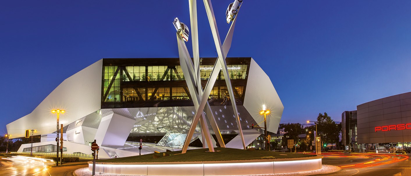 Das Porsche Museum bei Nacht mit einer beleuchteten Skulptur, auf der Autos montiert sind. Moderne Architektur und klare Linien dominieren das Bild., © Porsche AG Das Porsche Museum bei Nacht mit einer beleuchteten Skulptur, auf der Autos montiert sind. Moderne Architektur und klare Linien dominieren das Bild., © Porsche AG