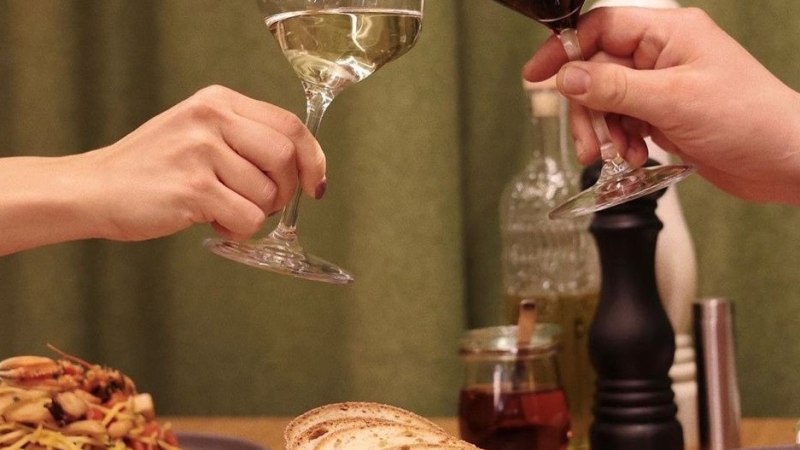 Two people toast with glasses of white and red wine, surrounded by pasta, bread and vegetable dishes on a table., © Roberts