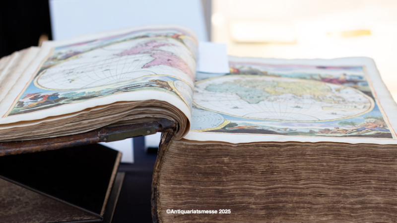 Ein altes Buch mit einer farbigen Weltkarte liegt aufgeschlagen auf einem Tisch, pr&auml;sentiert auf der Antiquariatsmesse 2025., &copy; Antiquariatsmesse, 2025