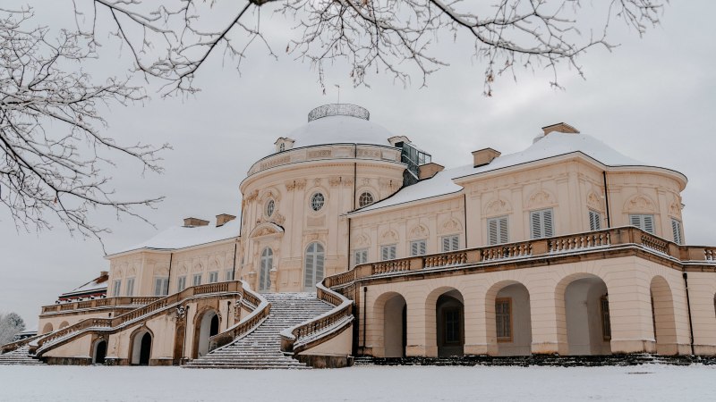 Solitude Palace in winter, covered in snow. A magnificent building with curved staircases and bare trees in the foreground., © SMG Thomas Niedermüller Solitude Palace in winter, covered in snow. A magnificent building with curved staircases and bare trees in the foreground., © SMG Thomas Niedermüller