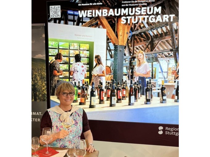 Frau mit Weinglas vor Plakat des Weinbaumuseums Stuttgart, das Weinflaschen und Besucher zeigt., © Stuttgart Marketing GmbH Frau mit Weinglas vor Plakat des Weinbaumuseums Stuttgart, das Weinflaschen und Besucher zeigt., © Stuttgart Marketing GmbH
