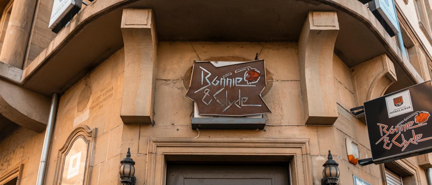 A sign with the inscription 'Bonnie & Clyde' hangs on a building. The façade is made of stone and there are decorative lanterns., © SMG Stuttgart Marketing GmbH - Sarah Schmid A sign with the inscription 'Bonnie & Clyde' hangs on a building. The façade is made of stone and there are decorative lanterns., © SMG Stuttgart Marketing GmbH - Sarah Schmid