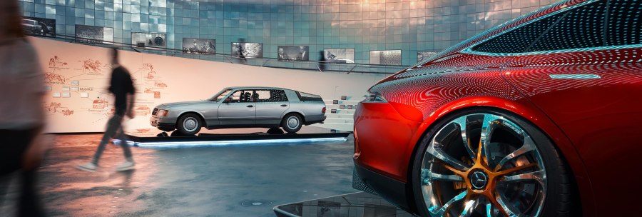 Innenansicht des Mercedes-Benz Museums mit einem roten und einem silbernen Auto. Besucher gehen vorbei, moderne Architektur und Beleuchtung im Hintergrund., © Mercedes-Benz Heritage GmbH