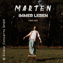 A man stands on a chair in a forest. Above it is written 'Marten Immer Leben Tour 2026'., © links im Bild A man stands on a chair in a forest. Above it is written 'Marten Immer Leben Tour 2026'., © links im Bild