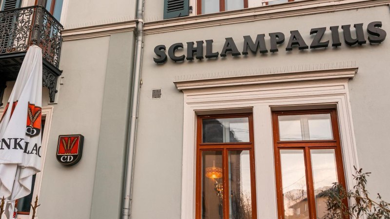 Fassade der Restaurant Kneipe mit dem Schriftzug 'Schlampazius', einem dekorativen Balkon und einem Sonnenschirm mit Logo., &copy; Stuttgart-Marketing GmbH, Sarah Schmid