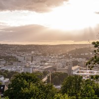 Blick von der Uhlandshöhe auf Stuttgart bei Sonnenuntergang. Die Stadt liegt unter einem dramatischen Himmel mit Sonnenstrahlen und Wolken., © Christine Garcia, Urban Trickytine Blick von der Uhlandshöhe auf Stuttgart bei Sonnenuntergang. Die Stadt liegt unter einem dramatischen Himmel mit Sonnenstrahlen und Wolken., © Christine Garcia, Urban Trickytine