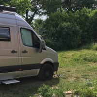 A silver motorhome stands on a green parking space. Trees and a rustic bench can be seen in the background., &copy; Weingut Idler