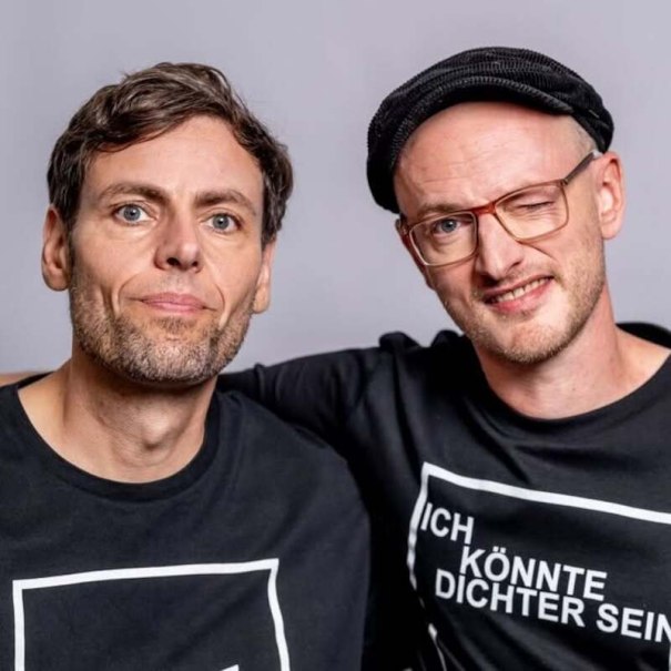 Two men in black T-shirts, one wearing a cap and winking. They pose in front of a neutral background., © Rosenau Kultur e.V. Two men in black T-shirts, one wearing a cap and winking. They pose in front of a neutral background., © Rosenau Kultur e.V.