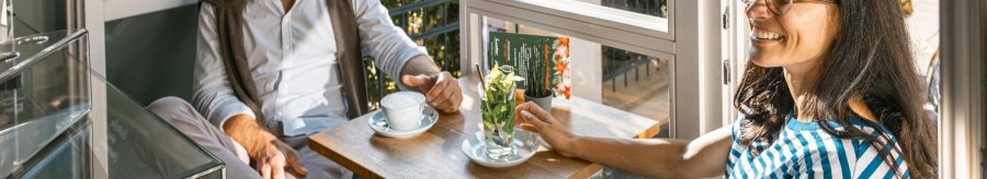 Zwei Personen sitzen in einem Caf&eacute; am Fenster, trinken Kaffee und unterhalten sich l&auml;chelnd. Sonnenlicht f&auml;llt durch das Fenster., &copy; Stuttgart-Marketing GmbH, Sarah Schmid
