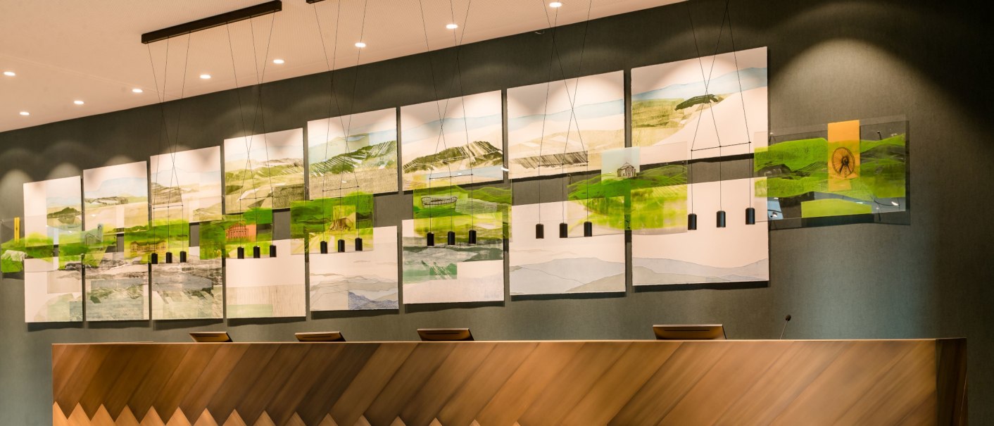 A modern reception with an artistic wall installation of landscape paintings and geometric shapes., © Motel One - Stuttgart Hauptbahnhof A modern reception with an artistic wall installation of landscape paintings and geometric shapes., © Motel One - Stuttgart Hauptbahnhof