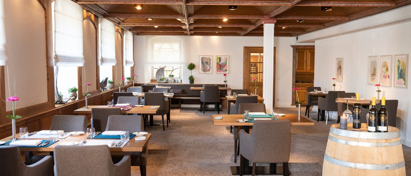 Elegant restaurant with wooden tables, gray chairs and a wine barrel. Bright windows and modern art on the walls create an inviting atmosphere., © Schlosshotel Monrepos Elegant restaurant with wooden tables, gray chairs and a wine barrel. Bright windows and modern art on the walls create an inviting atmosphere., © Schlosshotel Monrepos