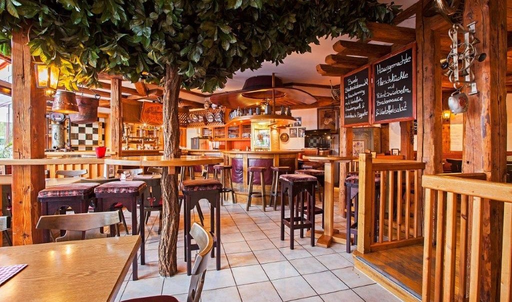 A cozy bar with wooden furniture, tree decorations, and chalkboards listing the menu items. The decor has a rustic and inviting feel., &copy; Hotel Waldhorn