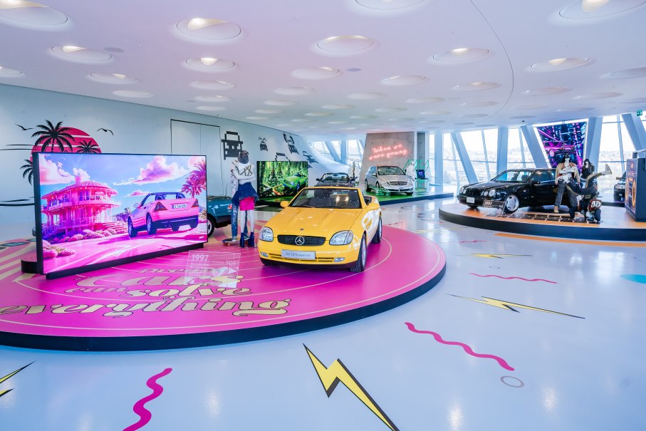 Bunte Ausstellung mit Youngtimer-Autos, darunter ein gelber Mercedes SLK. Neonlichter und Bildschirme mit Retro-Designs schmücken den Raum., © © Mercedes-Benz AG | Foto: Thomas Niedermüller Bunte Ausstellung mit Youngtimer-Autos, darunter ein gelber Mercedes SLK. Neonlichter und Bildschirme mit Retro-Designs schmücken den Raum., © © Mercedes-Benz AG | Foto: Thomas Niedermüller