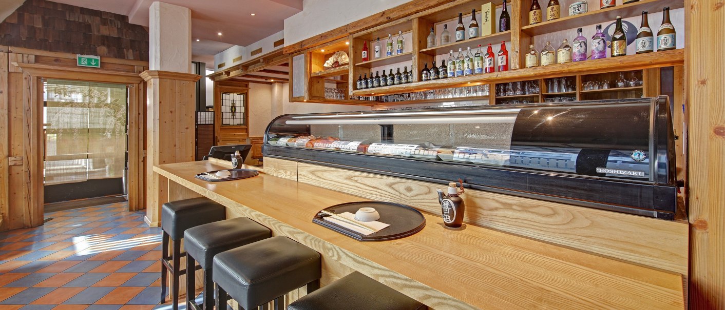 A Japanese restaurant with a sushi counter, bar stools and shelves full of sake bottles. Wooden elements dominate the interior., © Martin Frey