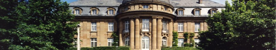 Die Villa Reitzenstein mit imposanter Fassade, einem Brunnen im Vordergrund und einer Flagge auf dem Dach, umgeben von B&auml;umen., &copy; Staatsministerium Baden-W&uuml;rttemberg