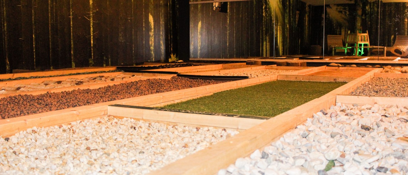 A barefoot park with different floor coverings such as stones and grass in a room with forest wallpaper., &copy; TOMAS