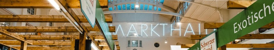 Interior view of the Stuttgart market hall with wooden stalls, illuminated signage and various delicatessen stalls., © by Canto