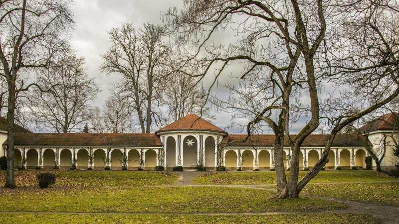 Historic spa house in Bad Boll with arcades, surrounded by bare trees and a green lawn in the foreground., © Stuttgart-Marketing GmbH, Sarah Schmid Historic spa house in Bad Boll with arcades, surrounded by bare trees and a green lawn in the foreground., © Stuttgart-Marketing GmbH, Sarah Schmid