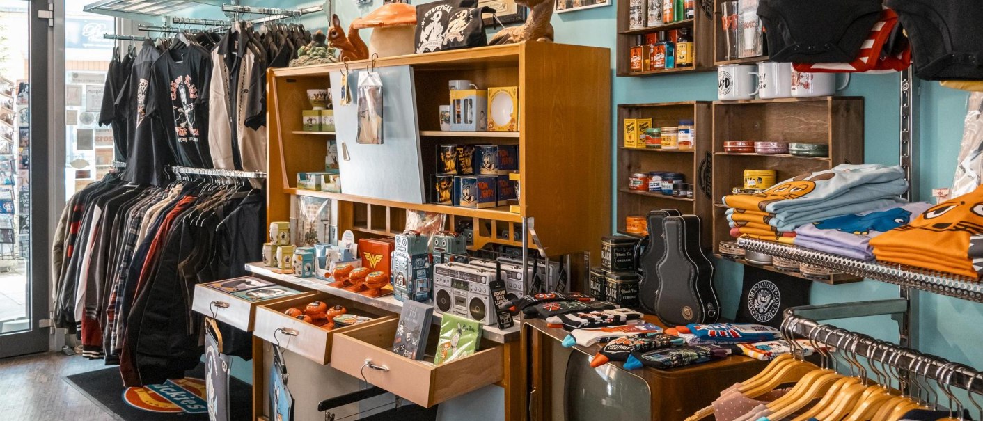 Ein Retro-Laden mit T-Shirts, Jacken und Vintage-Artikeln. Regale voller bunter Produkte und ein Kleiderständer mit verschiedenen Kleidungsstücken., © SMG, Sarah Schmid
