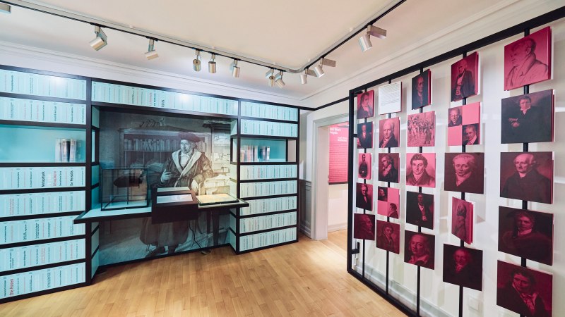 Ausstellungsraum im Hegel-Haus mit Bücherregalen, historischen Porträts und einer beleuchteten Vitrine auf Holzboden., © Julia Ochs Ausstellungsraum im Hegel-Haus mit Bücherregalen, historischen Porträts und einer beleuchteten Vitrine auf Holzboden., © Julia Ochs