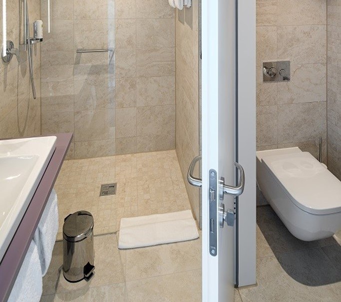 Modern bathroom with walk-in shower, washbasin and toilet. Light-colored tiles and a towel rail are visible., © Hotel am Remspark Modern bathroom with walk-in shower, washbasin and toilet. Light-colored tiles and a towel rail are visible., © Hotel am Remspark
