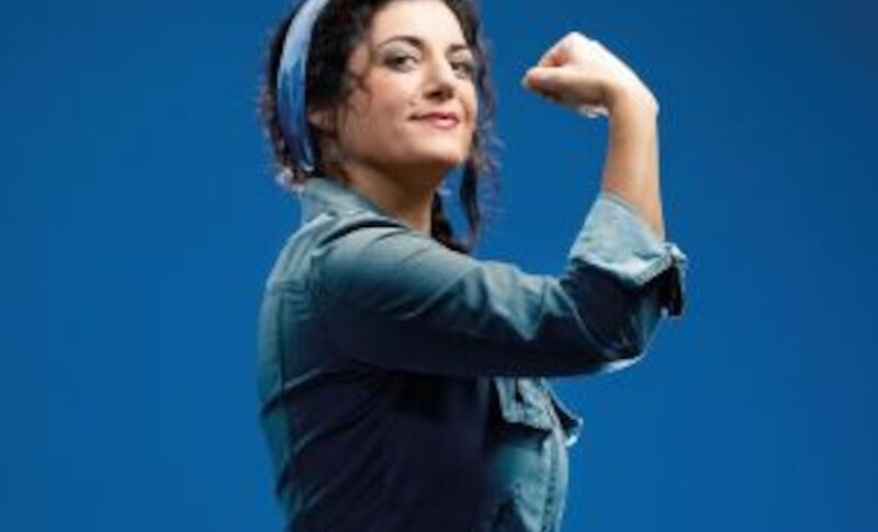 Frau in Arbeitskleidung mit Kopftuch zeigt eine starke Pose vor blauem Hintergrund, inspiriert von Rosie the Riveter., &copy; Altes Schauspielhaus und Kom&ouml;die im Marquardt e.V.