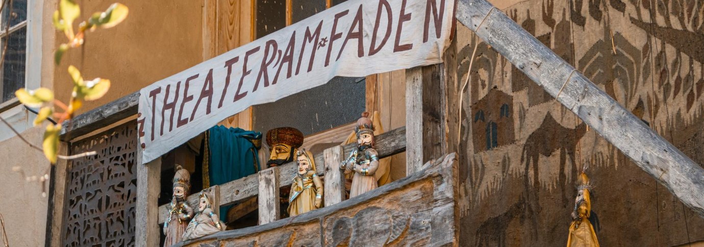 Ein Holzbalkon mit Puppen und einem handgemalten Banner 'Theater am Faden'. Die Puppen sind traditionell gekleidet., &copy; SMG, Sarah Schmid