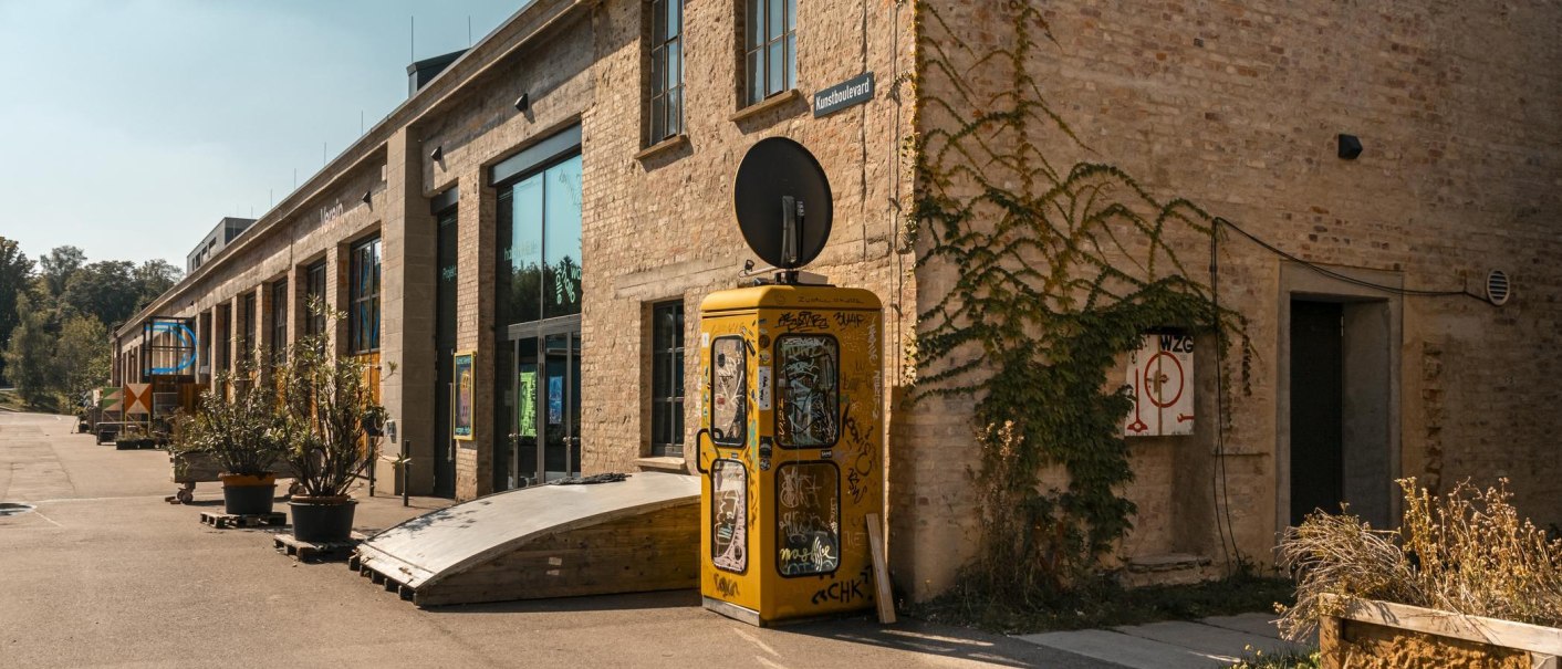 Altes Backsteingebäude mit großen Fenstern, gelber Telefonzelle und Pflanzen. Ein Schild mit der Aufschrift 'Kunstboulevard' ist sichtbar., © Stuttgart Marketing GmbH, Sarah Schmid