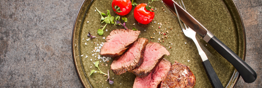 A plate with sliced steak, two cherry tomatoes and cutlery on a rustic base., © MAREDO
