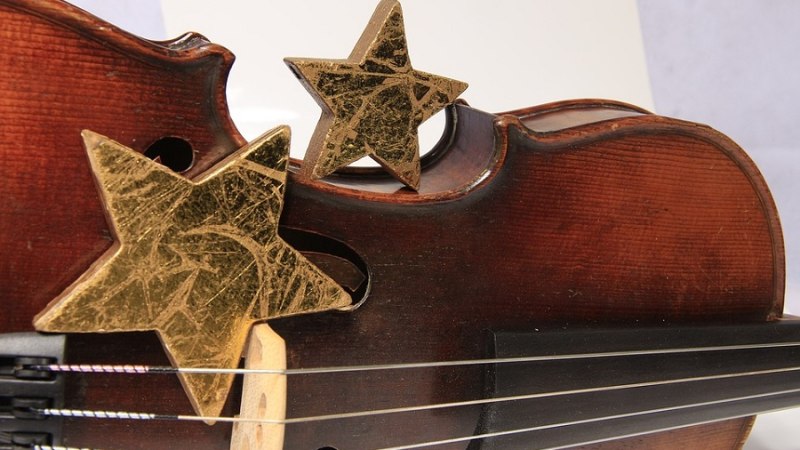 Nahaufnahme einer Geige mit zwei goldenen Sternen als Dekoration auf dem Korpus. Die Sterne verleihen der Szene eine weihnachtliche Atmosphäre., © Pixabay