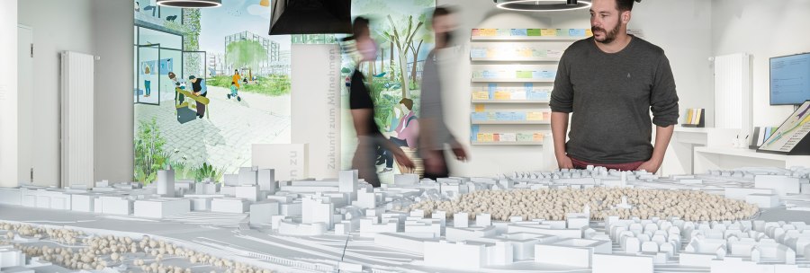 A man looks at an architectural model in an exhibition. Illustrations and notes can be seen on the wall in the background., &copy; Dominique Brewing